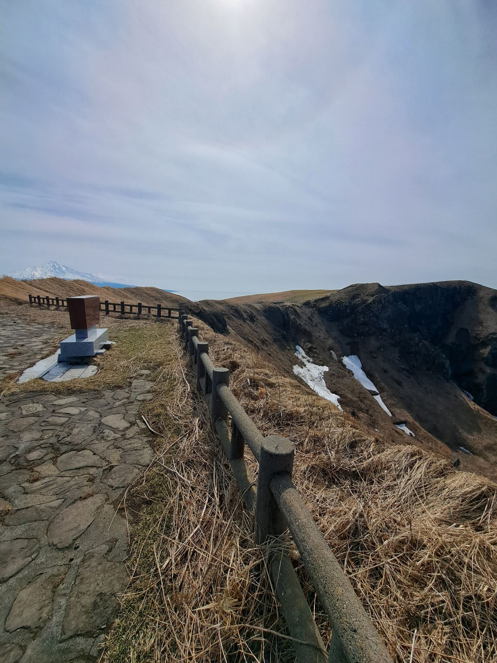 A stone path and wooden handrail along the plateau ridge, with patches of snow