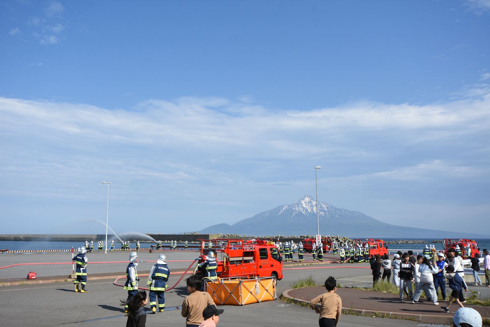 Firefighters and fire trucks on the pier, with snow-capped Rishiri behind